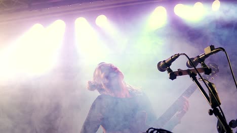 young beautiful female performer with a guitar singing on stage with colourful lighting background