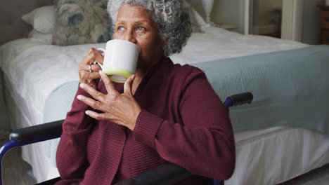 Senior-african-american-woman-sitting-on-the-wheelchair-drinking-coffee-at-home