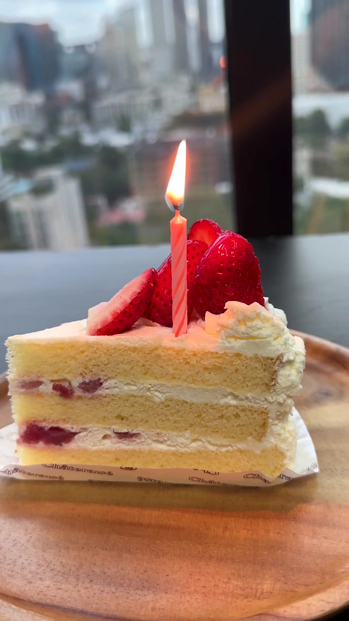 ろうそくが灯るいちごのケーキ一切れ、自然光、都市の背景、安定したクローズアップショット。