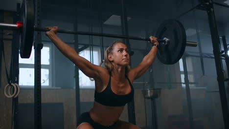 slow motion: training squats with barbells over head. muscular female lifting barbell over head training shoulders at gym. confident fitness woman practicing force workout with heavy equipment.