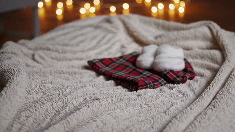 baby booties and plaid outfit on a fluffy bed with christmas lights