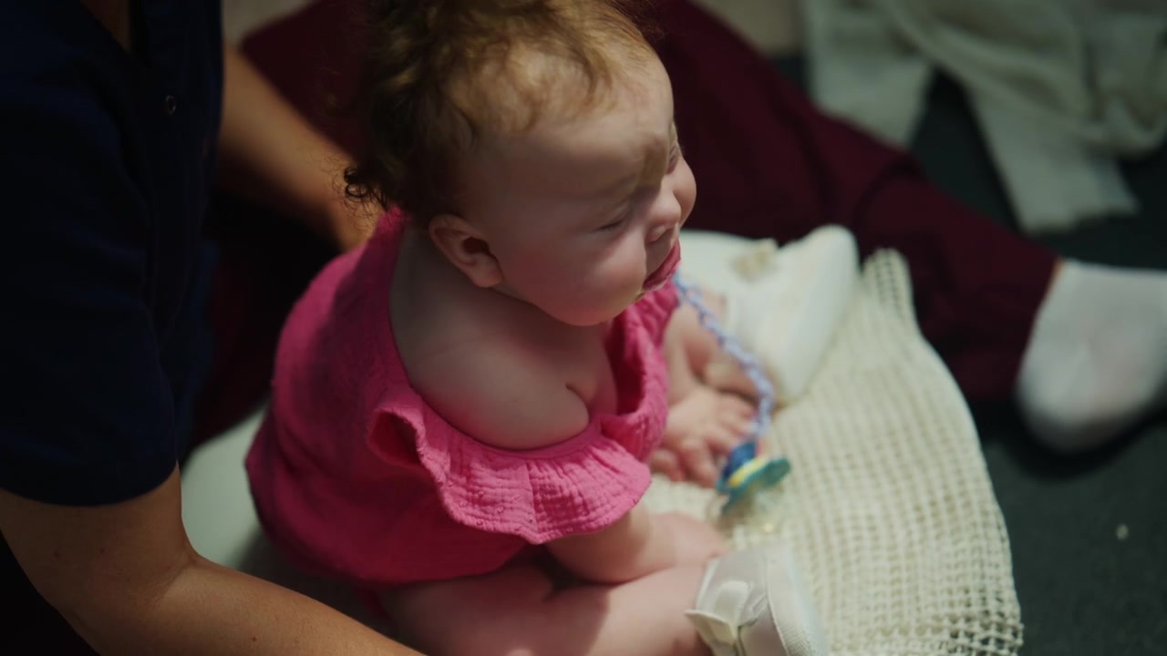 Overhead view of caregivers providing support while an infant is sitting on a white cloth