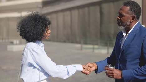 african businessman and businesswoman shaking hands outdoors