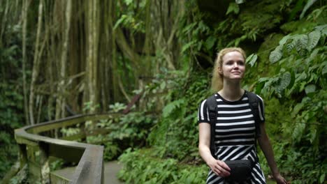 atractiva joven exploradora en un vestido blanco y negro que atraviesa la selva tropical en un camino de madera y un puente con mochila y mochila caminando con confianza ubud bali indonesia