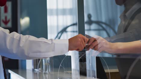 mixed race man and female receptionist wearing face masks at hotel reception desk