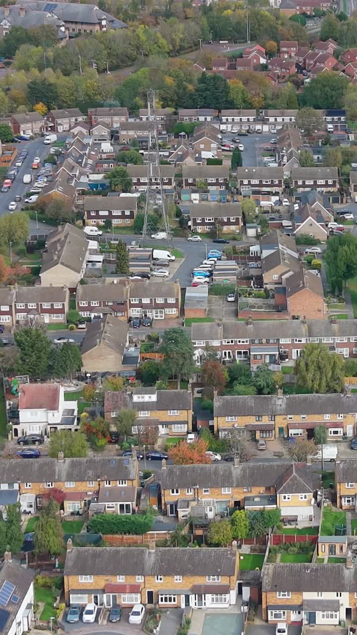 Vertical drone shot over Cheshunt, Hertfordshire, looking down at houses and an electricity pylon. The aerial establishing shot shows the residential area, greenery, and infrastructure in daylight