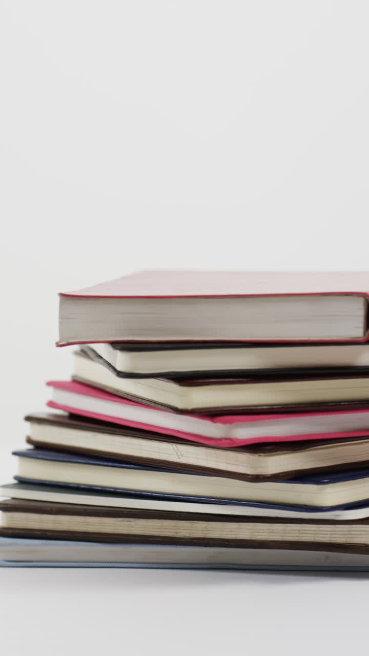 Vertical video of stack of books with copy space on grey background, in slow motion