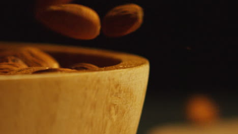 Primer-Plano-De-Almendras-Cayendo-En-Un-Recipiente-De-Madera-Contra-Un-Fondo-De-Estudio-Negro,-Filmado-En-Cámara-Lenta-1