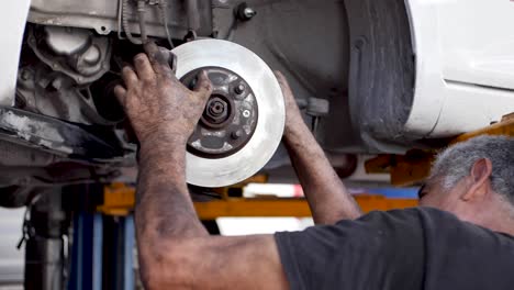 canoso mecánico mexicano ajustando el disco de freno de un automóvil recientemente rectificado para un cliente latino