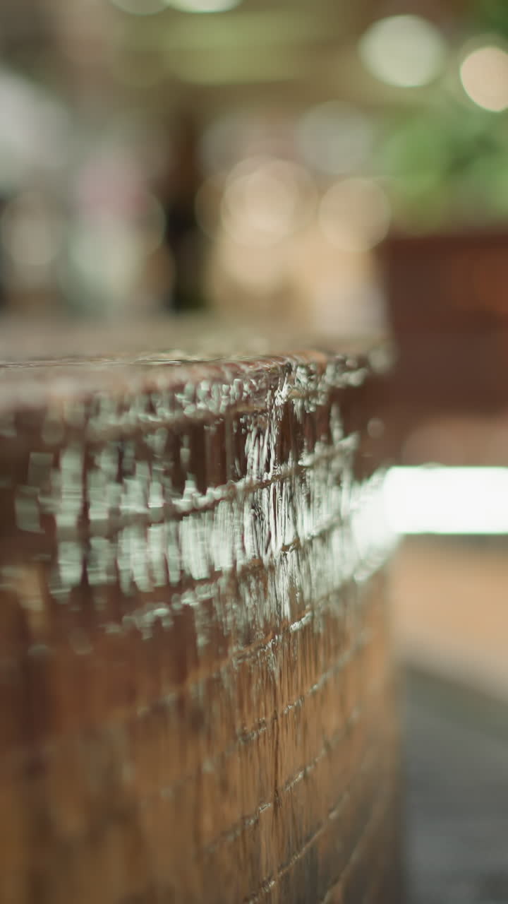 primer plano de agua en cascada por un borde de fuente texturizado y azulejos con fondo borroso con luz ambiental y un objeto colorido y poco claro