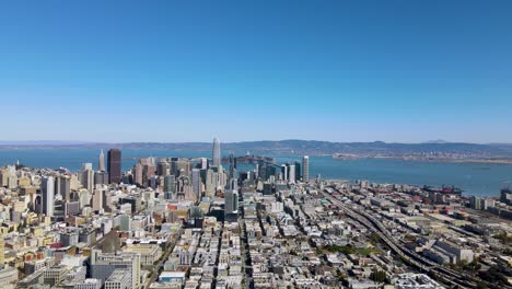 Aerial-view-of-San-Francisco-skyline-with-bay-bridge,-ocean-and-mountains-in-background,-Drone-Pan-Left