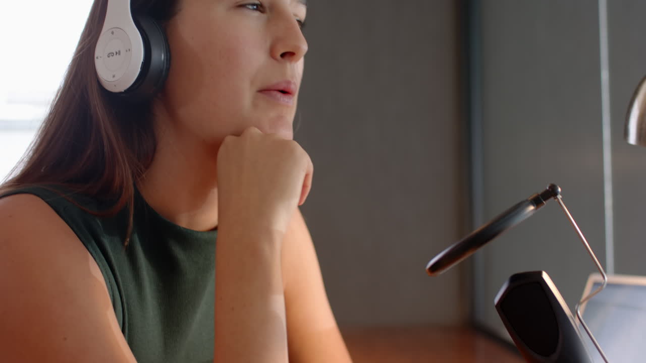 Wearing headphones, woman speaking into microphone, recording podcast at home