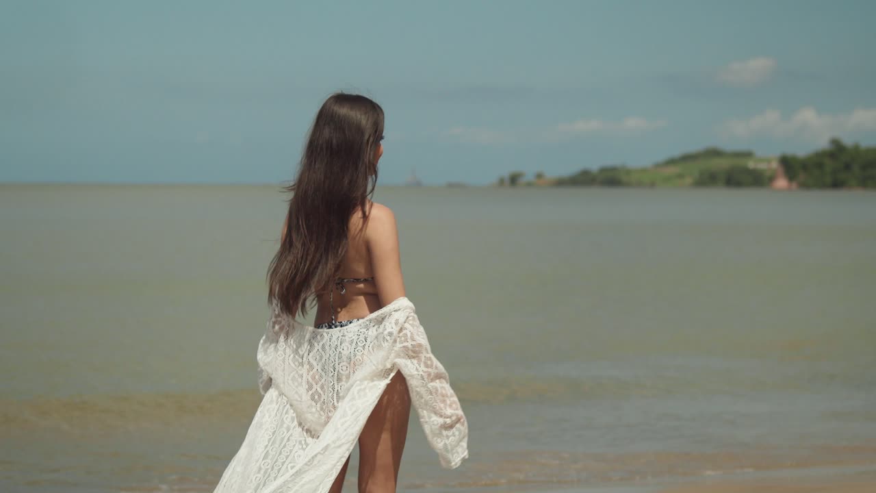 웃는 동안 화창한 날에 비키니 입은 해변에서 젊은 라티나 산책 및 회전