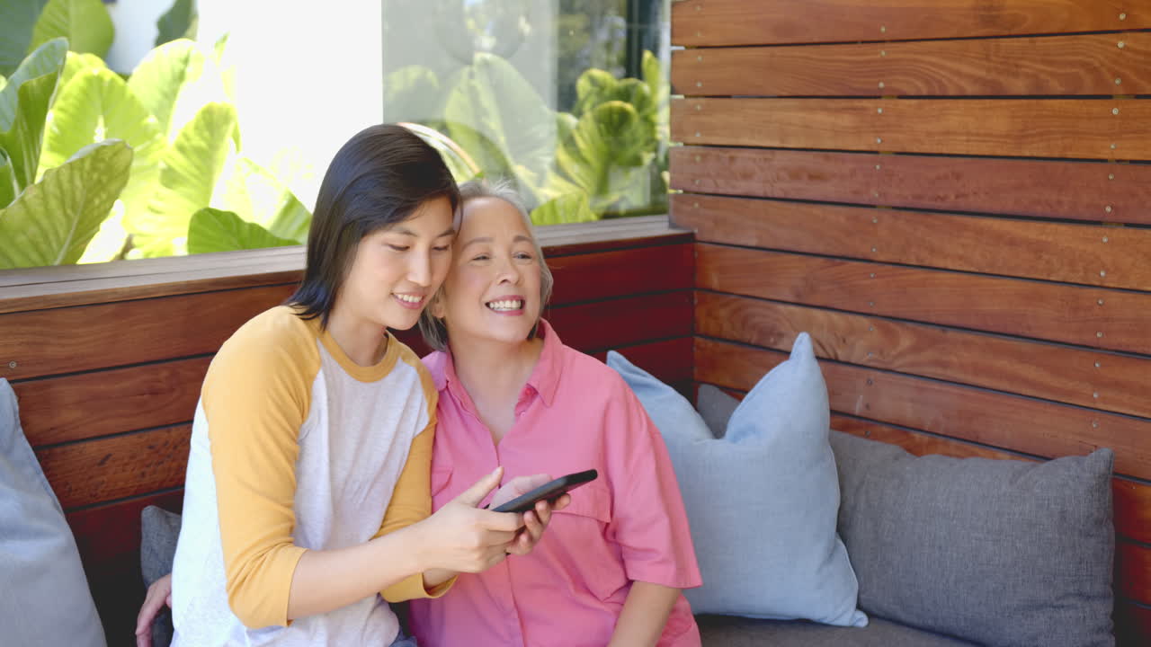 Smiling women sitting on couch, using smartphone and enjoying time together