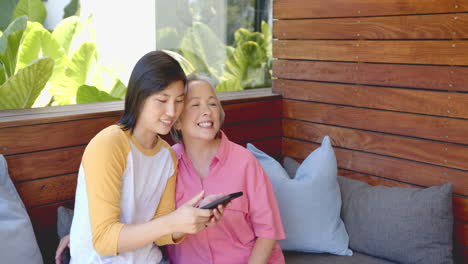 smiling women sitting on couch, using smartphone and enjoying time together