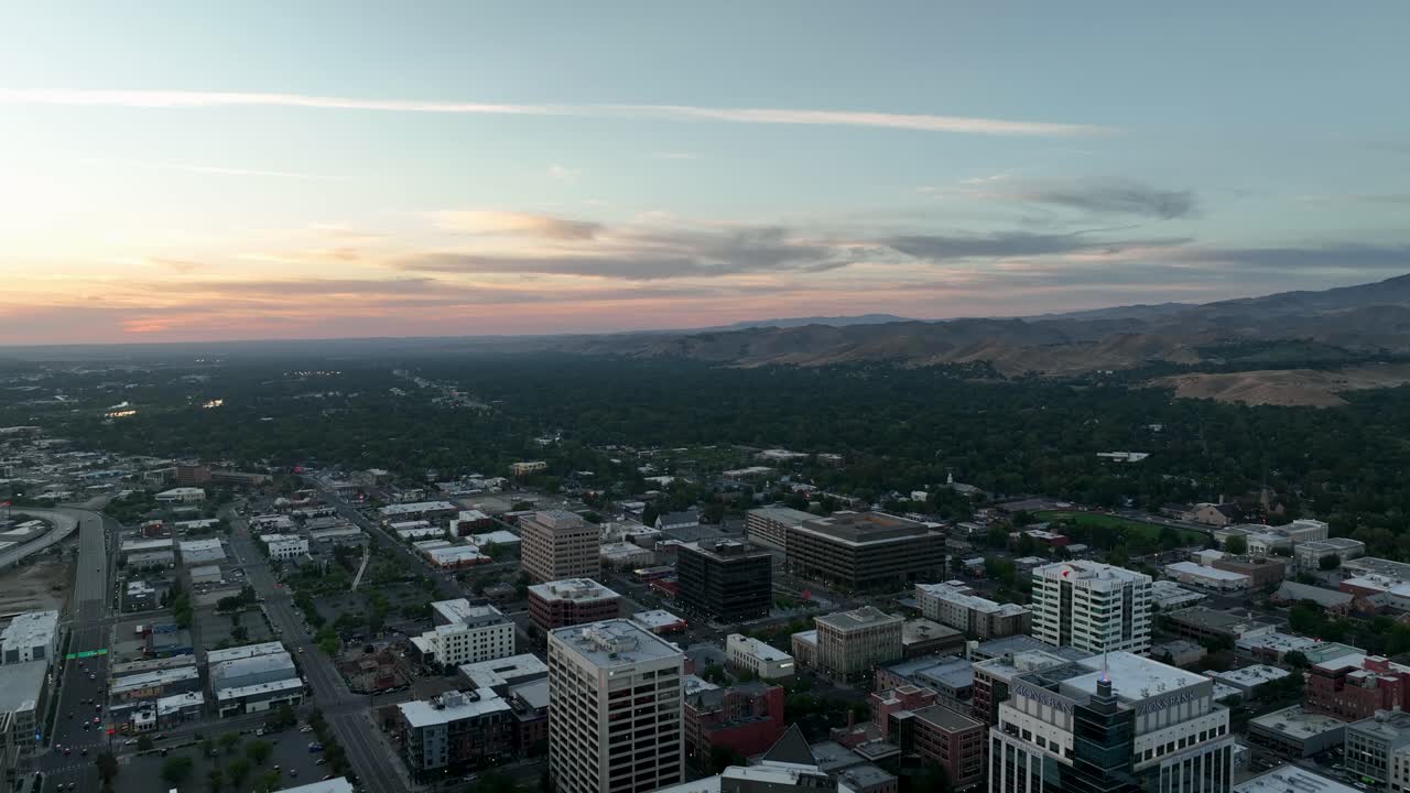 Aerial of Boise cityscape and river valley with forest and arid mountains at dusk