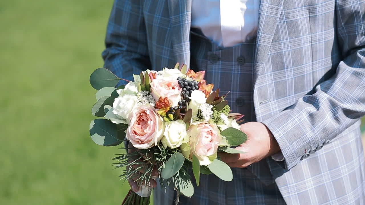 Sposo che tiene il bouquet da sposa. Giovane uomo con fiori