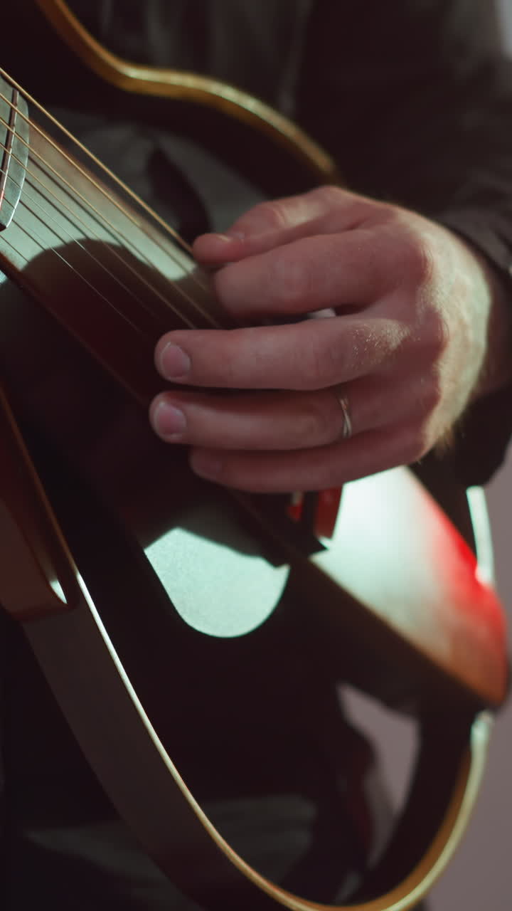 guitarrista sin rostro vestido de negro, tocando atentamente una guitarra roja, con un enfoque en las manos y las cuerdas en un entorno sutilmente iluminado. ideal para actuaciones musicales y contenido de técnica de guitarristas