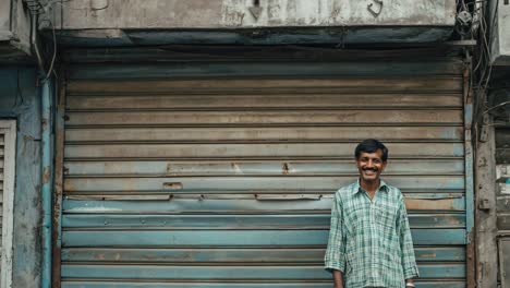 indian shopkeeper standing in front of the closed rolling shutter of his shop, probably during a holiday or a strike, in a typical street of india