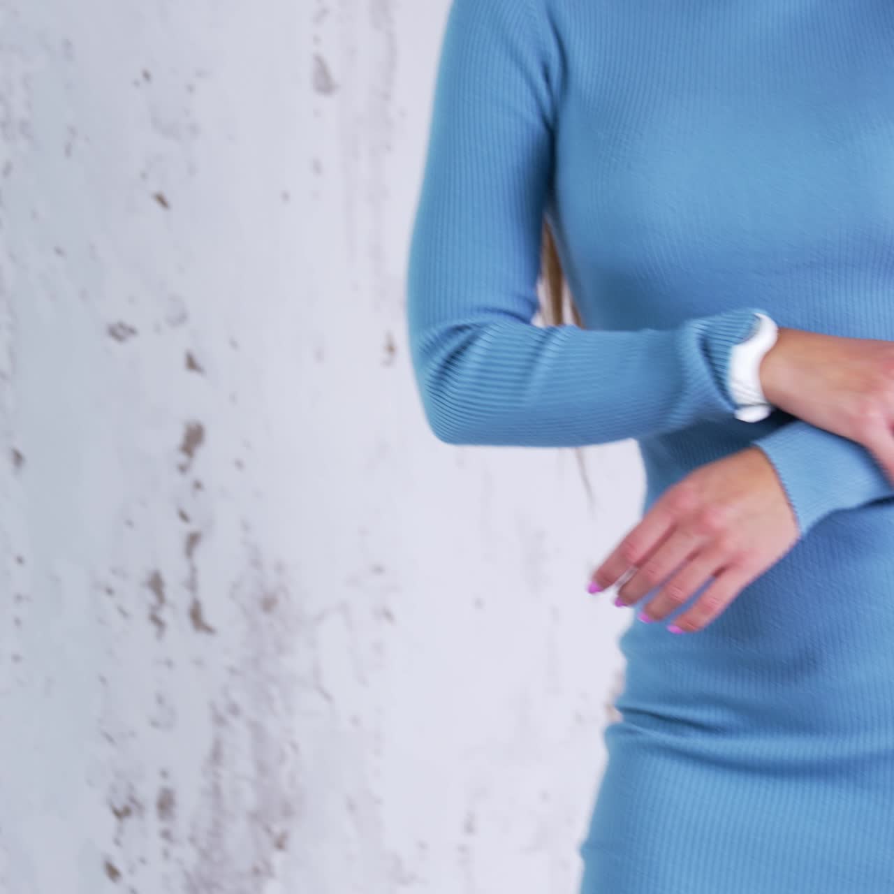 Beautiful long-haired woman in warm light blue dress indoors. Fashionable lady in tight dress and white boots on tractor soles. White backdrop