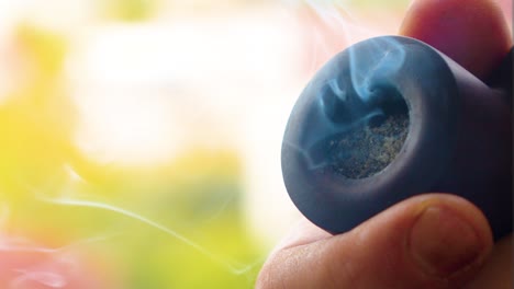 black pipe close up caucasian male smoking in the old style fashioned way antique vintage smoking device brought into 21st century producing blue shaded smoke visible finger tips of the smoker holding