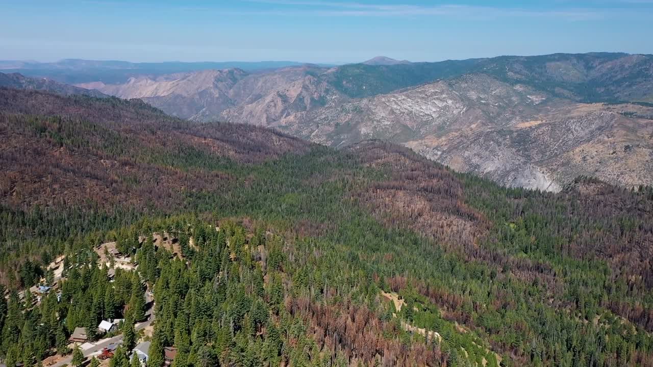 Aerial drone view showing Sierra Nevada foothills near Yosemite with dense forest, mountain slopes, and distant valleys under clear blue sky in California during sunny day