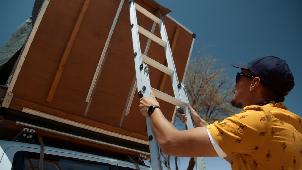 Handheld shot of a tourist as he lowers his rooftop canvas tent of his off road vehicle in Africa.