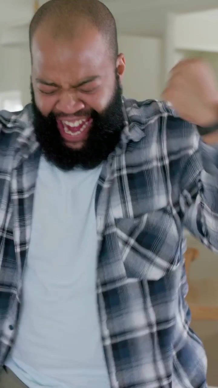 Vertical video: Shouting sparking bearded man in plaid pumping fists at home, grabbing green bottle