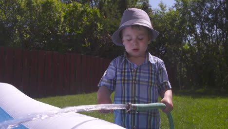 cute toddler boy splashing with water from a hose