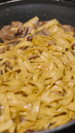 vertical video moving shot above italian mushroom tagliatelle resting in pan with various fungi including champignon, shitake, nameko. home cooked cream sauce based pasta dish.
