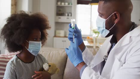 médico afroamericano con máscara facial llenando la jeringa con la vacuna contra la covid-19 en casa