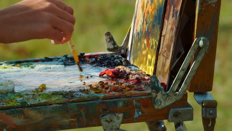 Painter-hands-drawing-picture-on-easel-closeup.-Artist-mixing-paints-on-palette.