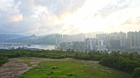 Eine-Dynamische-Luftaufnahme,-Die-Von-Den-Bergen-Aufsteigt-Und-Das-Stadtbild-Der-Neustadt-Tseung-Kwan-O-Zeigt,-Umgeben-Von-Verschiedenen-Wolkenkratzern-Und-Wunderschönen-Wolkenformationen-Bei-Sonnenuntergang