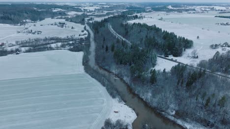 Vista-Aérea-Del-Valle-Del-Río-Abava-En-Un-Día-Nublado-De-Invierno,-Campos-Cubiertos-De-Nieve,-Río-Abava-Lleno-De-Agua-Oscura-De-Inundación,-Amplio-Disparo-De-Drones-Avanzando