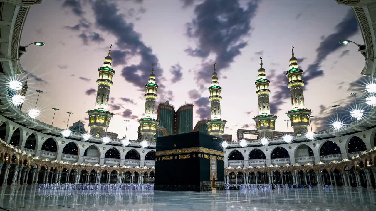 Wide-angle video shot of the Kaaba at dusk, capturing the illuminated minarets and dramatic sky