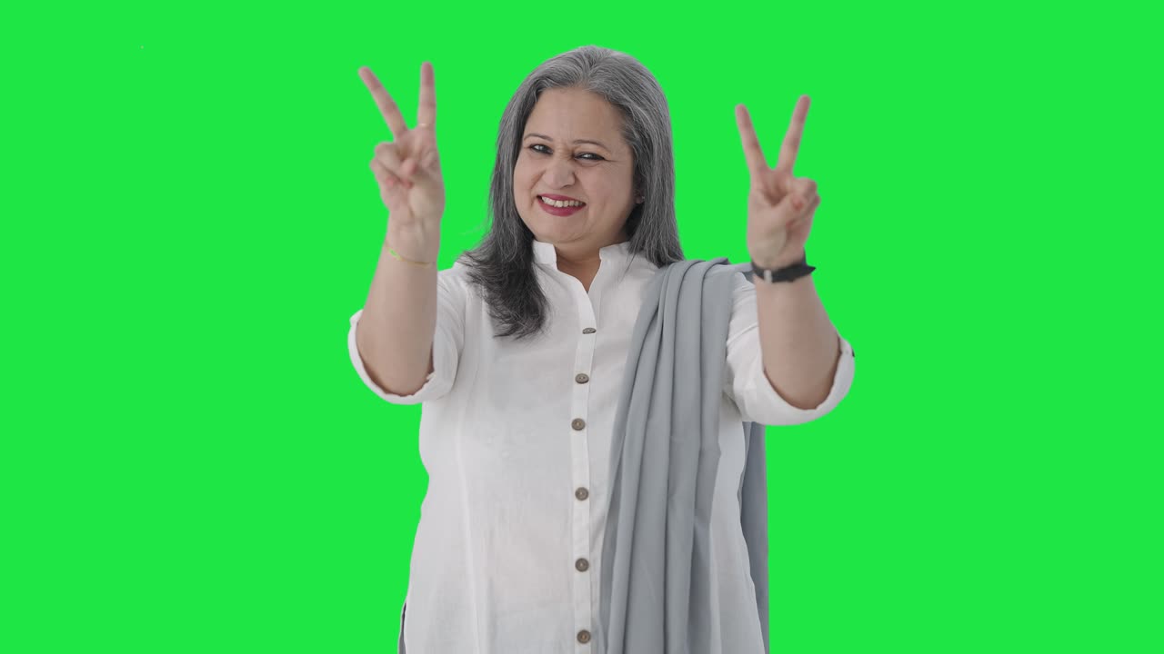 feliz mujer de negocios india senior mostrando el signo de la victoria pantalla verde