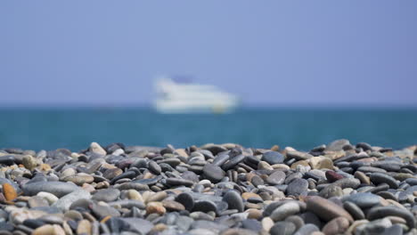 pebbles on sunny beach with blurry ship at sea panning left to right