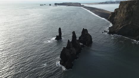 drone down tilt over reynisdrangar seastacks by reynisfjara black sand beach