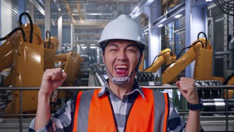 close up of asian male engineer with safety helmet screaming goal celebrating working with industrial robotic arms working