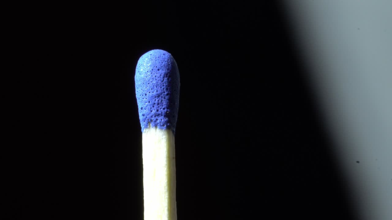 Close-up macro shot of blue match head with light and shadow movement, creative closeup with dark background