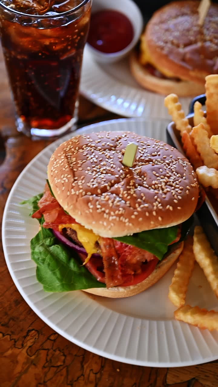 Juicy burger with fries and cola on rustic wooden table. Fresh cheeseburger with bacon, lettuce, and cheese served with fries and cola drink in cafe