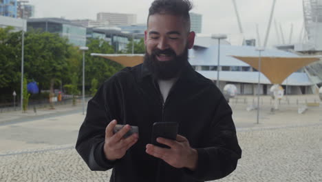 Hombre-Barbudo-Sonriente-Escribiendo-El-Número-De-Tarjeta-En-El-Teléfono-Inteligente-Al-Aire-Libre.