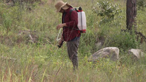 wide long shot of a man working with a backpack sprayer