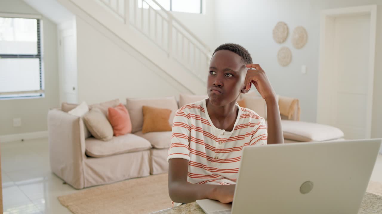 Male youth sitting at counter, studying on laptop, facing issue, pausing then relaxing into smile
