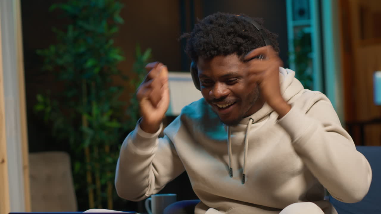 African american male person listening to a podcast and multitasking on the coffee table, browsing the internet and navigating through his laptop with headphones on. Self employed man. Camera A.