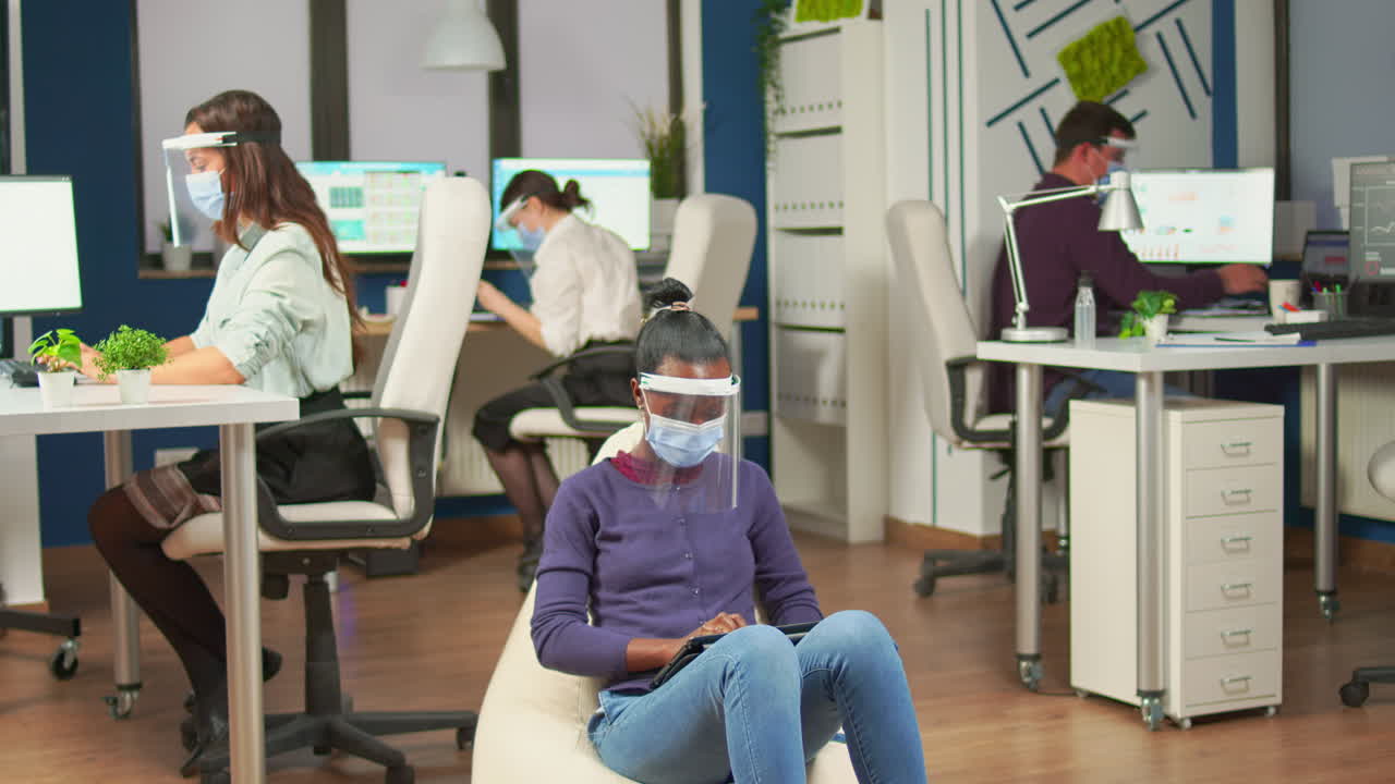 empleado africano con una tableta sentado en un sillón en la habitación de la oficina