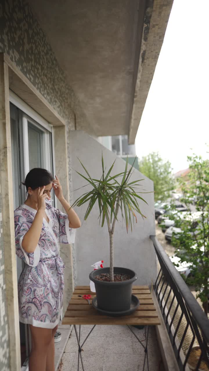 Woman Watering a Plant on a Balcony