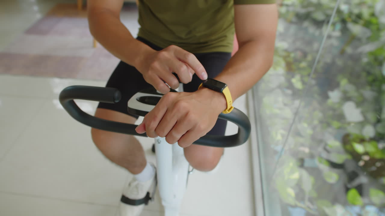 Unrecognizable Athlete Checking Fitness Bracelet during Training on Fitness Bike