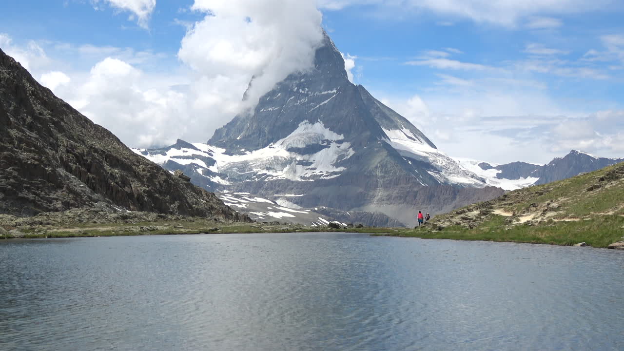 Weitwinkelaufnahme eines ruhigen Alpensees mit dem Matterhorn-Gipfel, der über felsigen Hängen und Schneeflecken nahe Zermatt, Wallis, Schweiz, an einem hellen Tag aufragt.