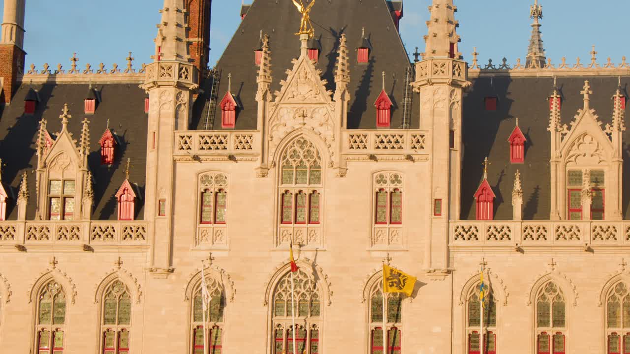 Camera slowly pans across historic Gothic city hall facade in Bruges, Belgium, during golden hour